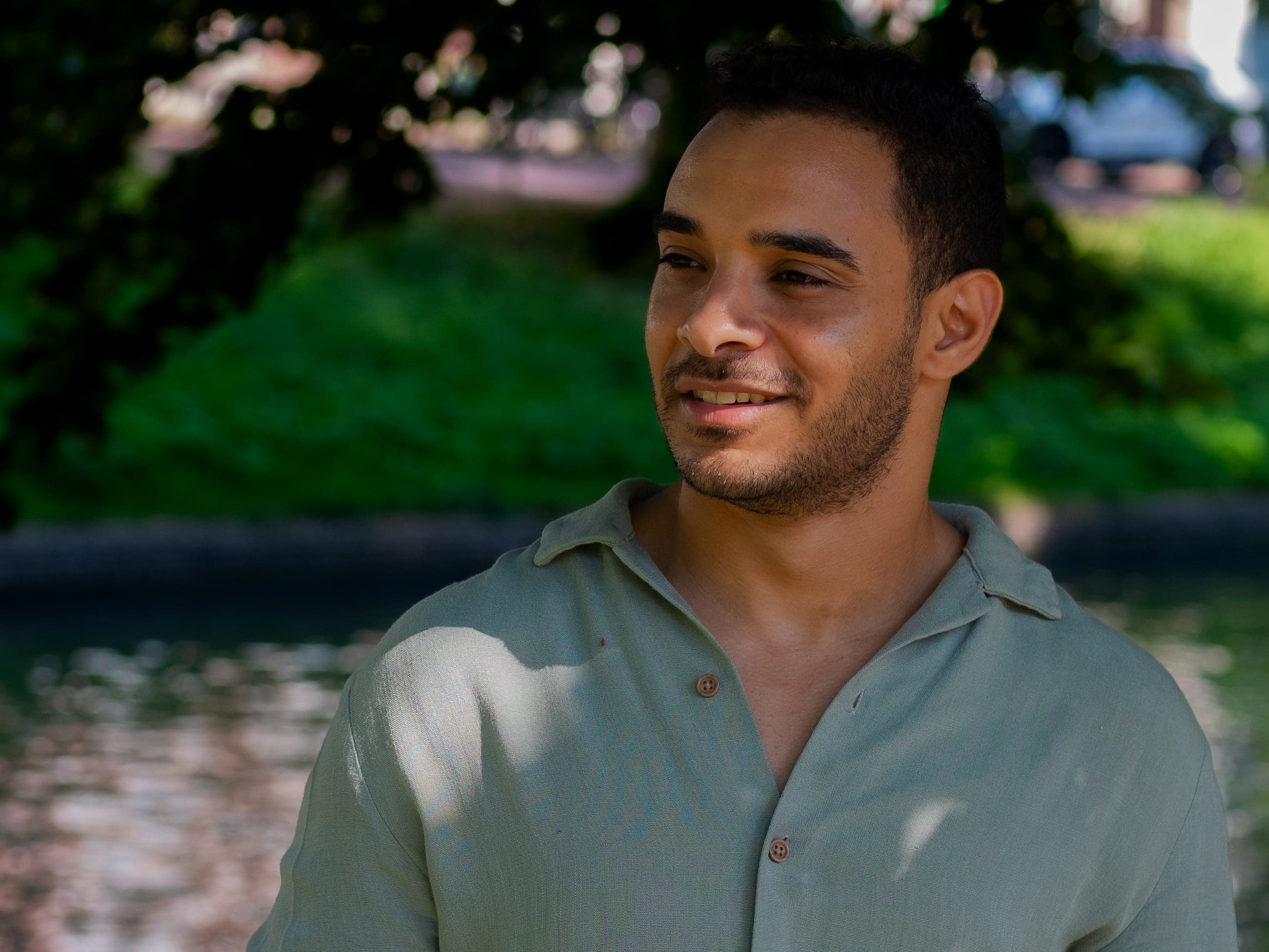 A portrait of Hithem, wearing a green shirt with a serene river flowing in the background.